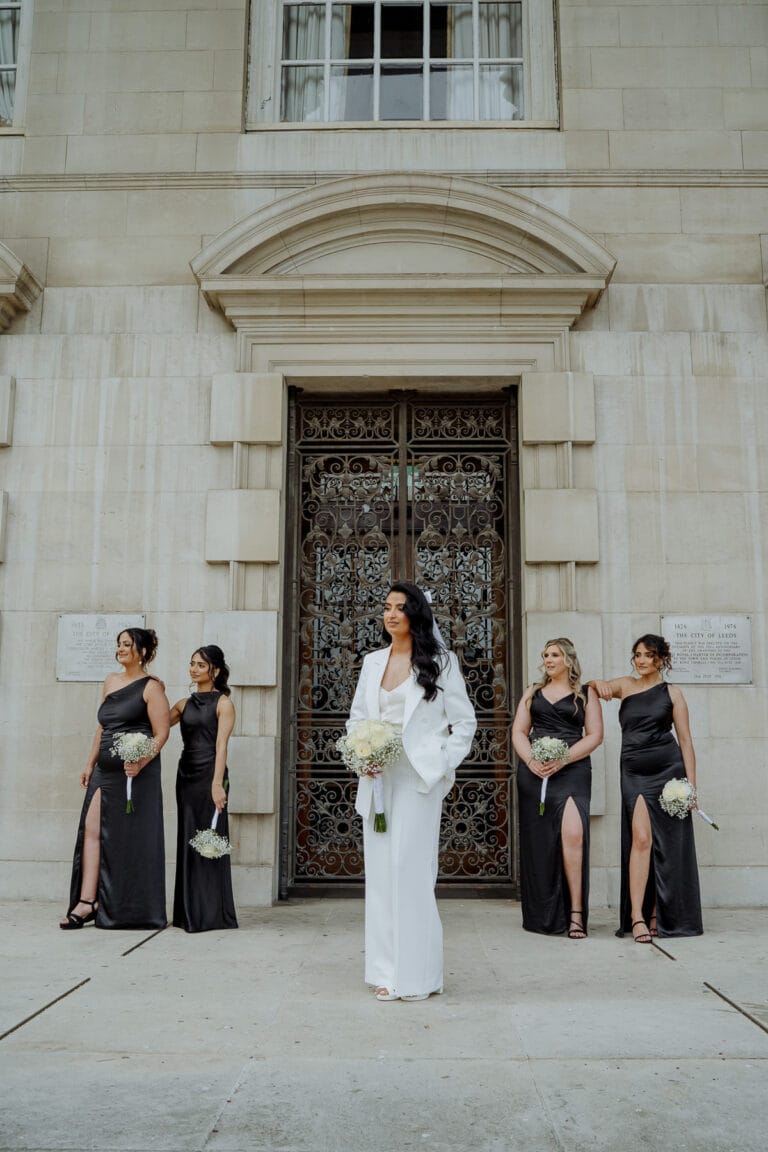 bride in white trouser suit with bridesmaids in black satin gowns at leeds civic hall wedding