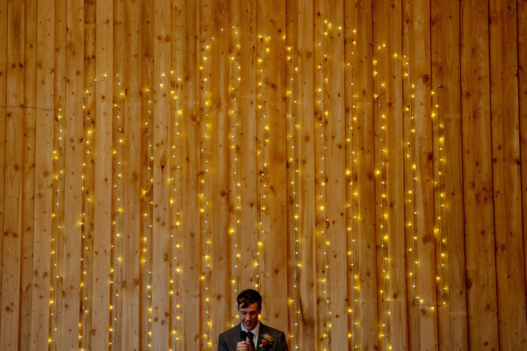 groom in front of fairy lights during speeches at lodge farm wedding venue cundall